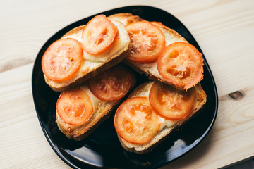 sandwiches with cheese and tomatoes are on a black plate. wooden background