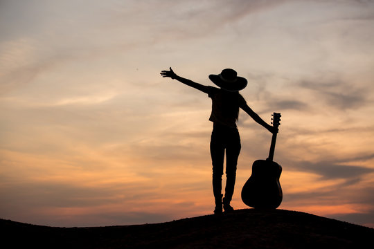 Silhouette of woman with guitar on the sunset