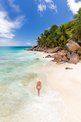 Fototapeta na wymiar Woman wearing retro striped bikini and beach hat, enjoying amazing view on Anse Patates beach on La Digue Island, Seychelles. Summer vacations on picture perfect tropical beach concept.