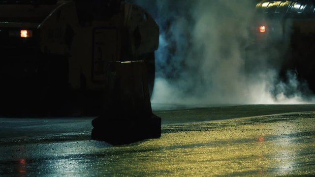 Roadworks at night. Steam rises from the hot asphalt. Rollers tamped new asphalt.