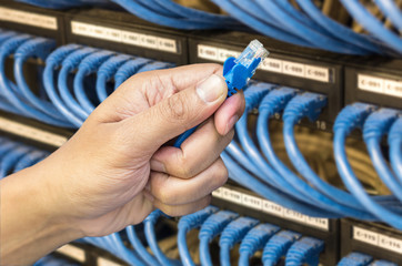 hand holding network cable on the switch hub in server room back
