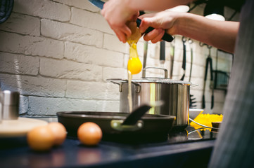 woman housewife prepares fried eggs with ham and vegetables in his kitchen. egg breaks, adding to the pan