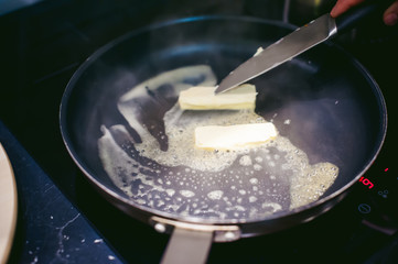 woman housewife prepares fried eggs with ham and vegetables in his kitchen. spreads the butter in the pan