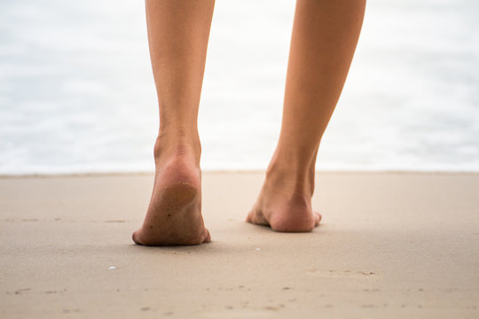 Low angle behind woman walking barefoot on beach