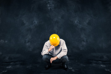 黒い背景で作業服を着て座り込む男性