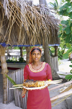 Maldivian woman offering a plate of grilled fish, Maldives