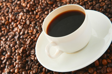 Cup of coffee on beans as background