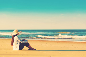 Fototapeta na wymiar Woman in a hat sitting on the beach