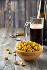 Salted pistachios with saffron and  glass of beer on old wooden background. Rustic style. Selective focus.