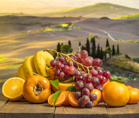 composition of fruits on wooden table on background Tuscan countryside