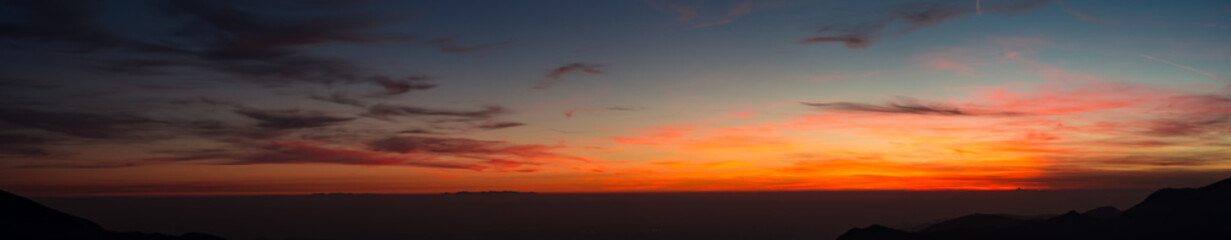 Fiery sunset from mountain pick with thin glazes in the sky evening. Fall season. Orobie alps. Rena pick. Bergamo Italy. In the distance the Monviso.