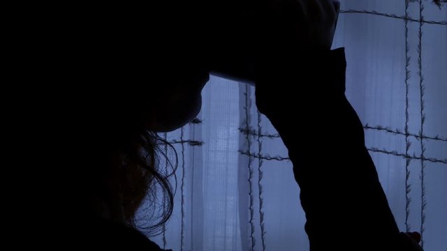 woman alone in a dark room sips and holds a cuo of tea