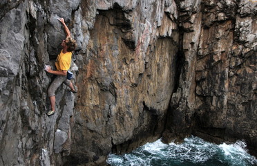 A climber deep water soloing above the sea on the limestone cliffs near St. Govan's Head, South Pembrokeshire, Pembrokeshire Coast National Park, Wales