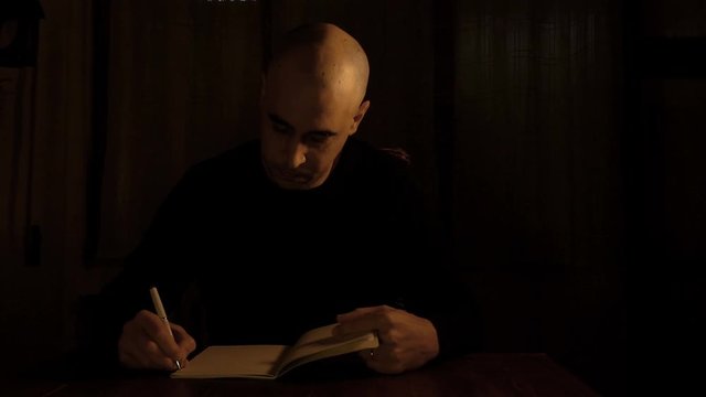 man sat alone in dark scene is writing some notes on his book