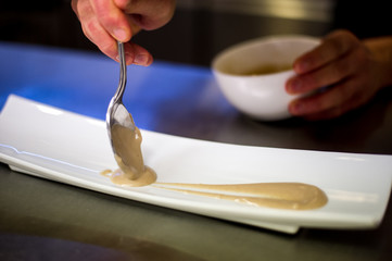 Fototapeta na wymiar Chef garnishing a long square dish with a spoon full of cream