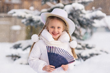 cheerful girl with a fan in his hand and a hat in the winter holiday is happy and laughs