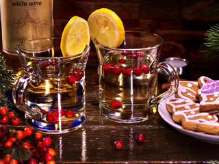Two mugs with Christmas drink, decorated with lemon, standing on wooden table. Christmas cookies and bottle wine with label.