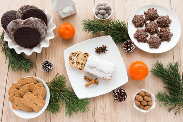 Arrangement of Gingerbread, Spiced Biscuits and Mini Christstollen on light wooden background surrounded by Christmas decoration.