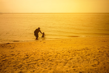 Silhouette image of father playing with his son in the sea in golden hour 