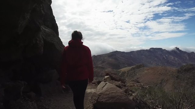 Young female hiker on a mountain trail. Camera is following a hiker in red jacket.