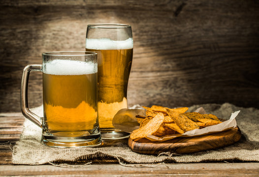 Beer in mug, glass on wooden table with and chips