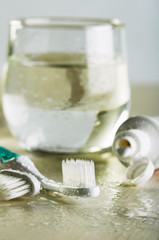 two toothbrushes, toothpaste and a glass of water on a wet table