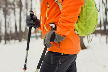 Hiker wearing backpack and hardshell jacket, skiing poles on hike in winter forest. The concept of modern equipment and clothes for tourism and recreation