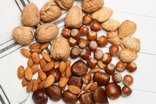 Avellanas, nueces, almendras y casta&ntilde;as naturales sobre una tabla de madera blanca con una servilleta. Vista superior