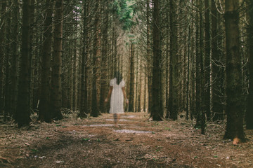 Female ghost walking barefoot through the forrest in white dress