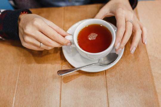 Hot mug of tea with woman hands in retro woollen sweater on wooden table