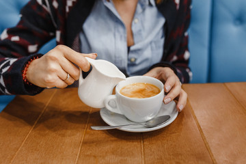 Woman pouring milk in mug of tea from kettle