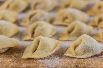 Freshly prepared Italian tortellini on wooden board  close up