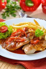 Deftiges Zigeunerschnitzel mit Pommes Frites vor roten Paprikaschoten - Hot escalope with red pepper sauce and French fries