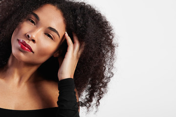 black woman with afro hair touches it and watching at camera