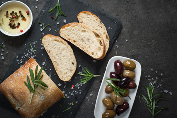 Italian ciabatta bread  on black slate with herbs and olives.