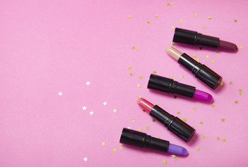 Assorted color lip stick cosmetics on a bright pink background with gold glitter stars and blank space at side