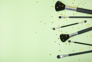Cosmetic make up brushes arrange on a pastel green background with gold stars and blank space at side