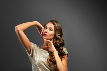 Fototapeta premium Glamorous young woman with wavy hair and red lipstick posing elegantly in golden sequin top, she wears a golden sequin top against a dark studio background