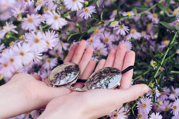Manos de una chica joven sosteniendo unas gafas de sol retro entre un montón de flores moradas 