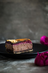 Piece of dark chocolate mousse cake with rose petal and blackberry jam on a black plate and stone background. Vegan, sugar, gluten free, dairy dessert. Vertical. Copy space