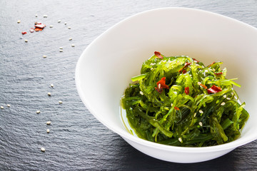 Traditional japanese chuka wakame salad with sesame seeds in white bowl on black stone.