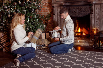 Obraz premium Young couple examines the gifts under Christmas tree. Holiday