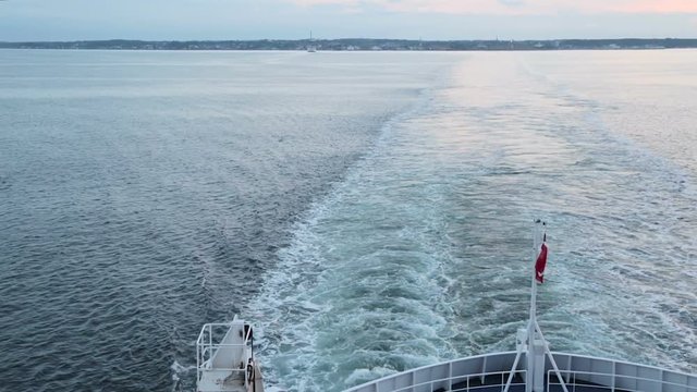 Danish flag fluttering in the wind on the stern of the ship. The ferry sails from Denmark to Sweden and back. Train on the water after the ship. Panorama shot from the bottom up to the top of the deck