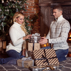 Young couple examines the gifts under Christmas tree. Holiday