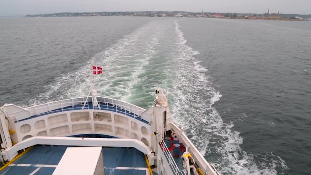 Danish flag fluttering in the wind on the stern of the ship. The ferry sails from Denmark to Sweden and back. Train on the water after the ship. Panorama shot from the bottom up to the top of the deck