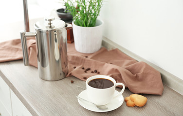 Cup of coffee with cookies and coffee pot on kitchen table
