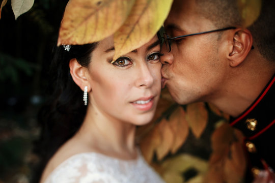 Bride kisses groom in uniform of US Army standing behind autumn