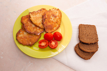 Potato pancakes with meat and tomatoes on green plate with rye b