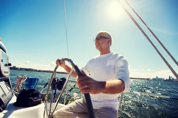 Fototapeten Senior Mann am Ruder auf Boot oder Yacht Segeln im Meer © Syda Productions
