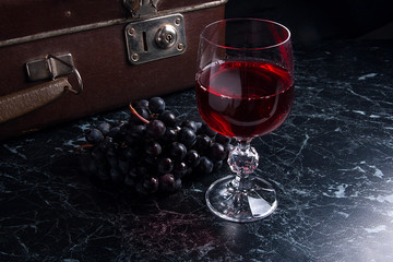 Glass of red wine on dark marble background. Cluster of blue gra